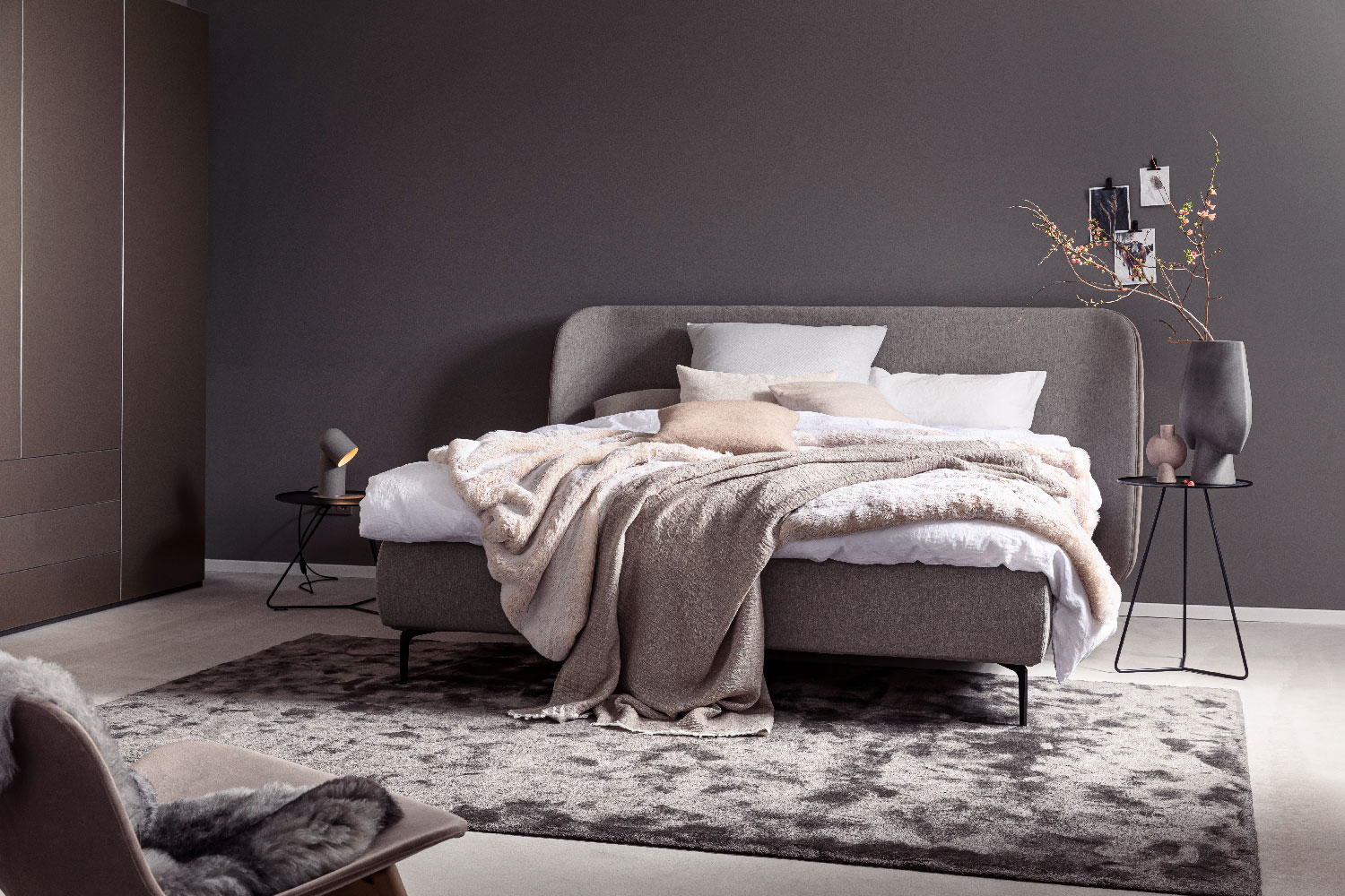 Ein stilvoll eingerichtetes Schlafzimmer mit Bett, Teppich und Beistelltischen in warmen Grau- und Pudertönen.