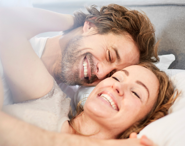 Ein glücklich lächelndes Paar liegt im Bett.