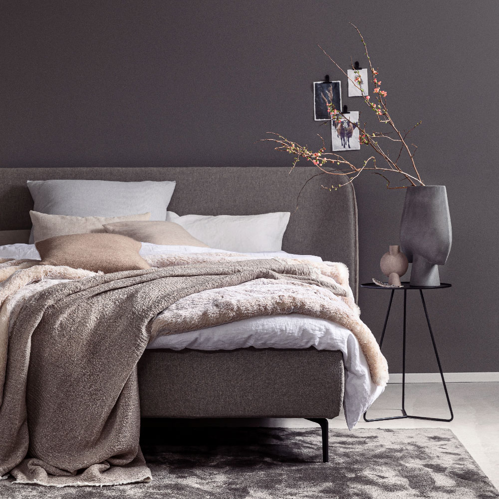 Ein stilvoll eingerichtetes Schlafzimmer mit Bett, Teppich und Beistelltischen in warmen Grau- und Pudertönen.