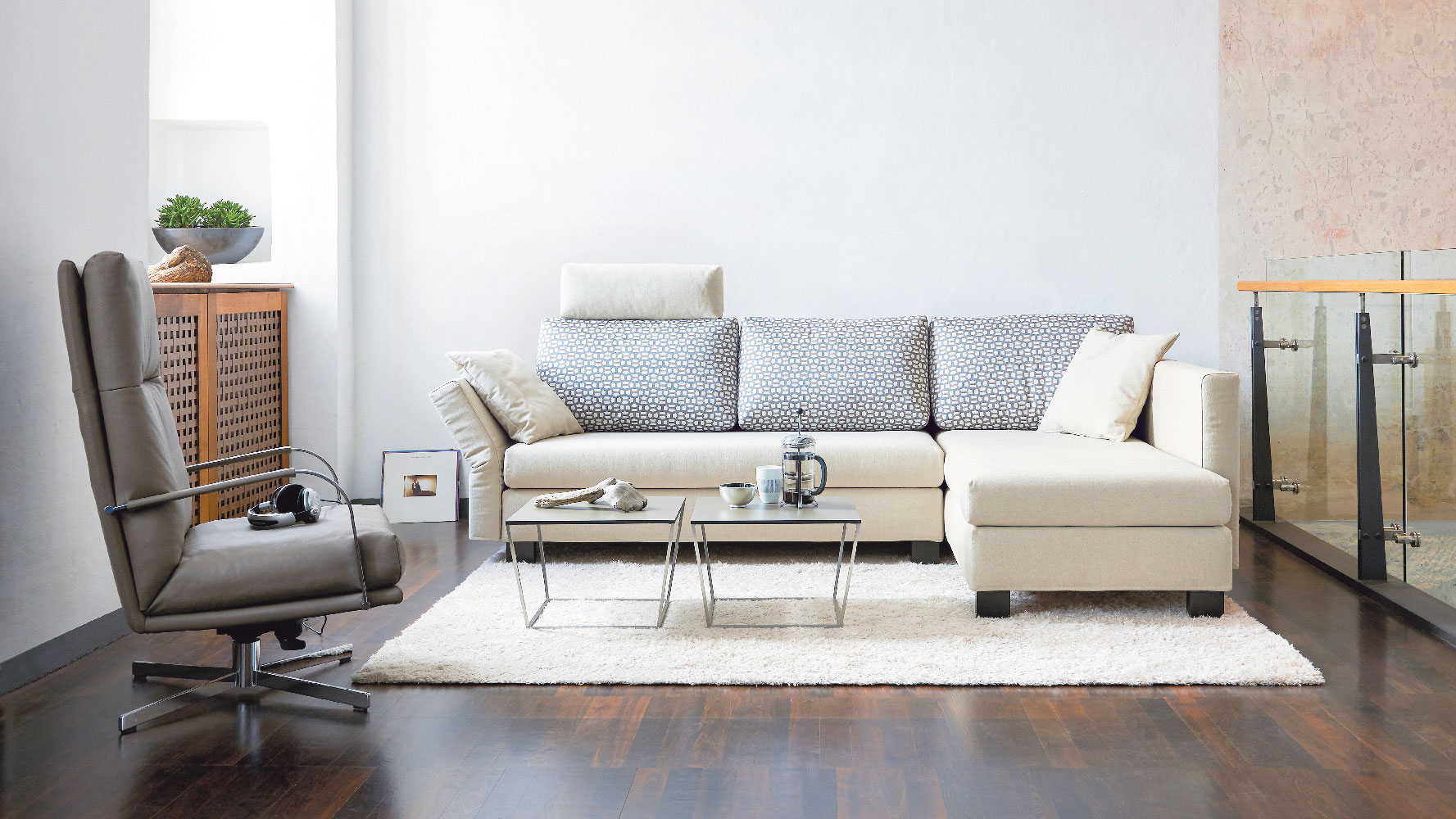 Modernes Wohnzimmer mit beigem Schlafsofa, Relaxsessel und Couchtisch auf einem hellen Teppich